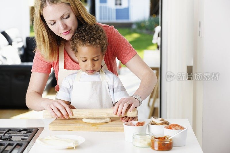 白人妇女/母亲协助混血儿卷披萨面团